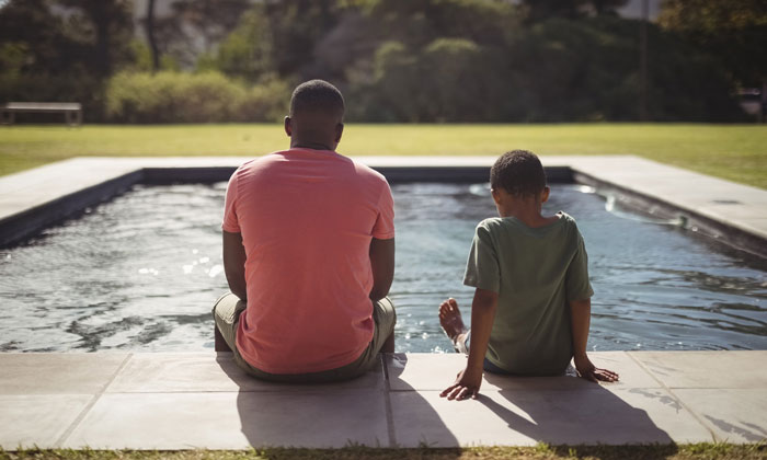 father and son sitting beside outdoor swimming pool