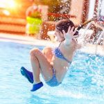 girl jumping into swimming pool with eyes closed